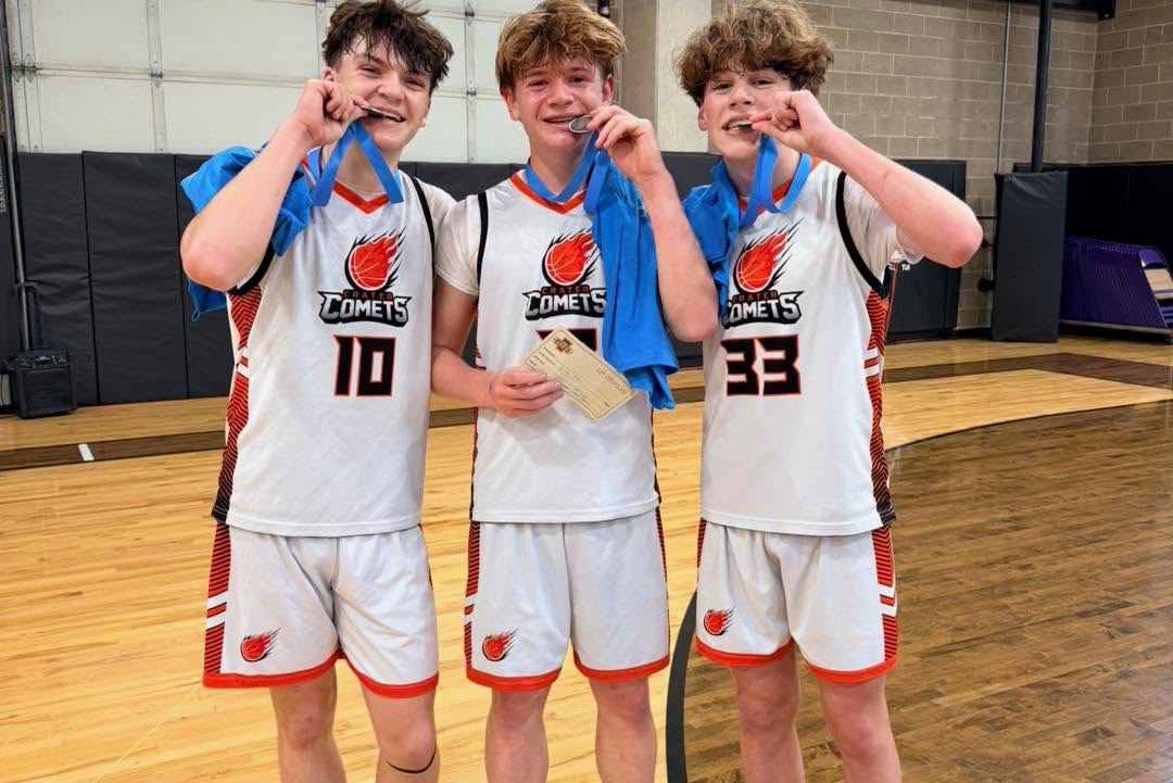 Three teenage basketball players in white Crater Comets uniforms celebrating with medals after the Gamerosity Superhero Classic 3v3 tournament.