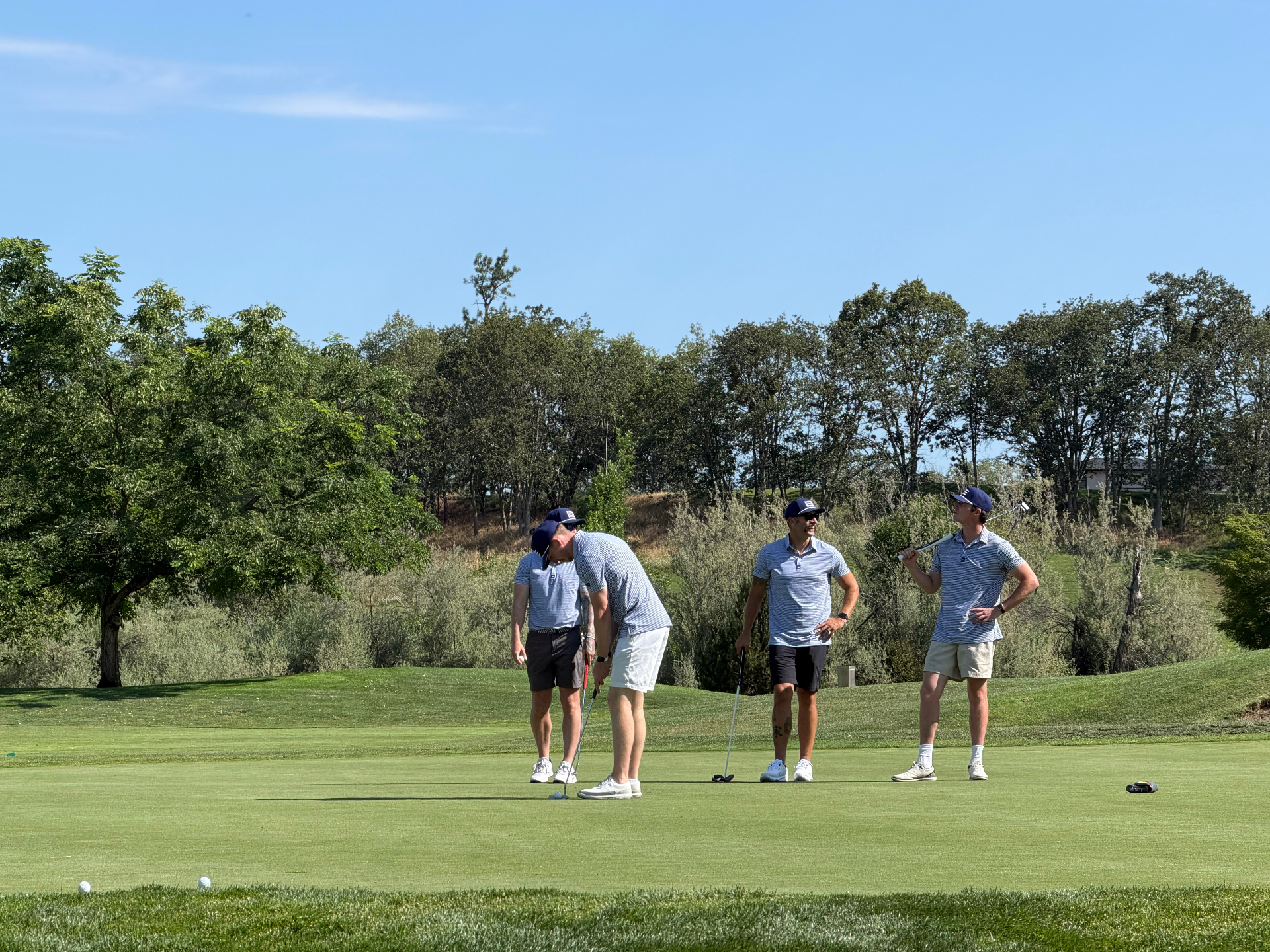 Four golfers in matching light blue Forte Clothing polos on the putting green during the Gamerosity Superhero Open golf tournament.